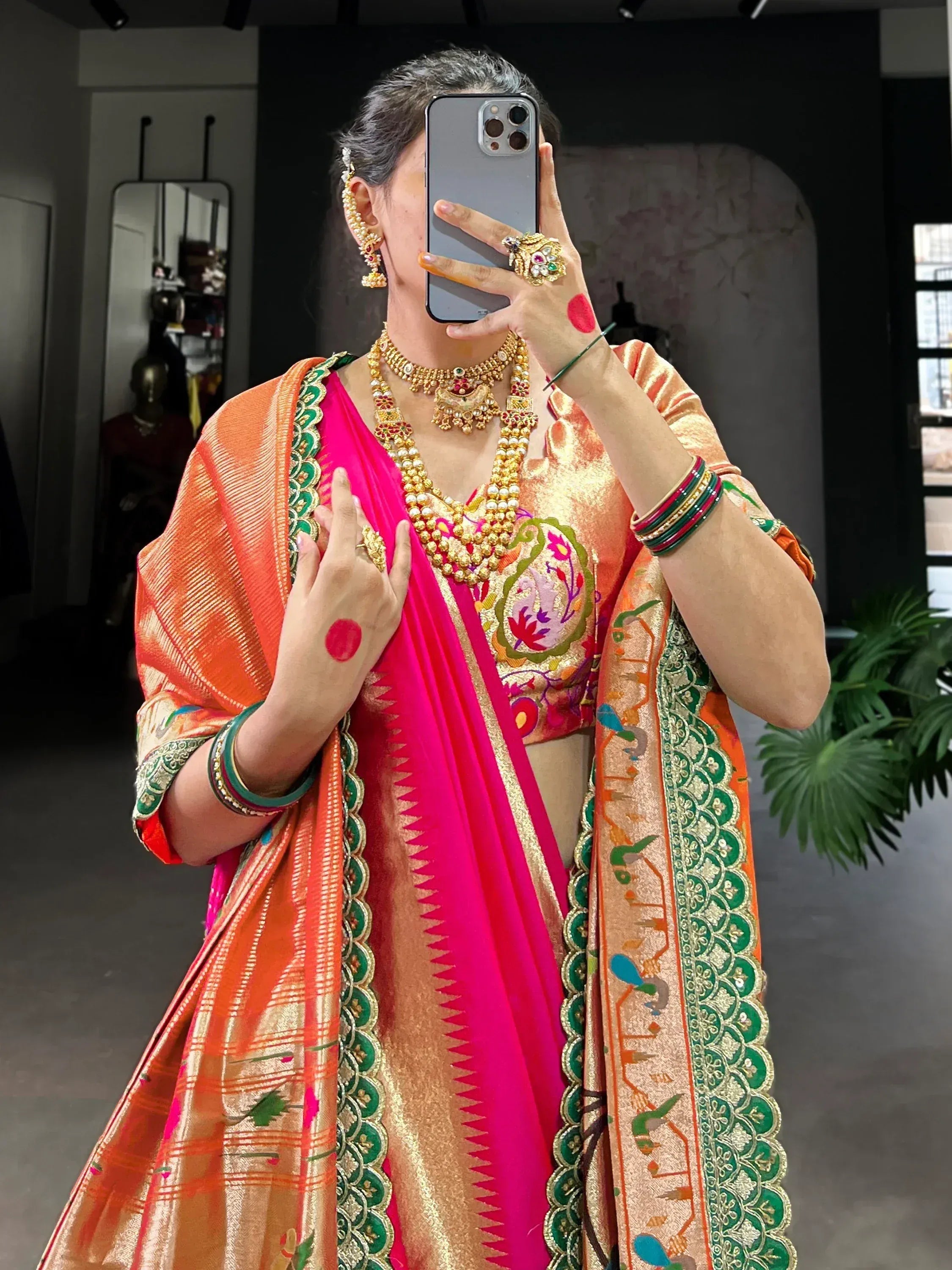 Woman in vibrant pink and orange designer saree with gold jewelry, capturing mirror selfie