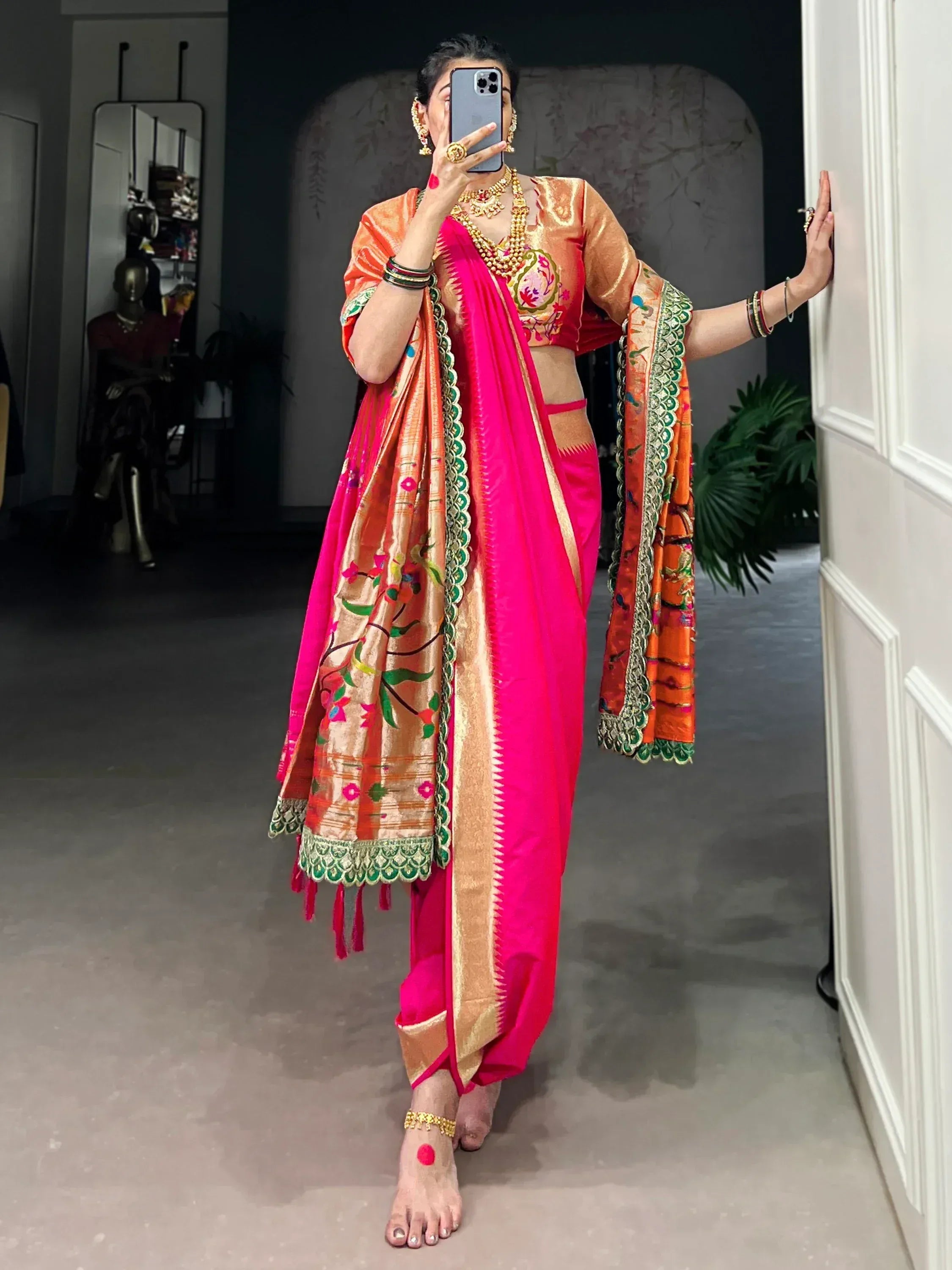 Vibrant pink and orange embroidered saree with floral motifs and gold border, styled with traditional jewelry.
