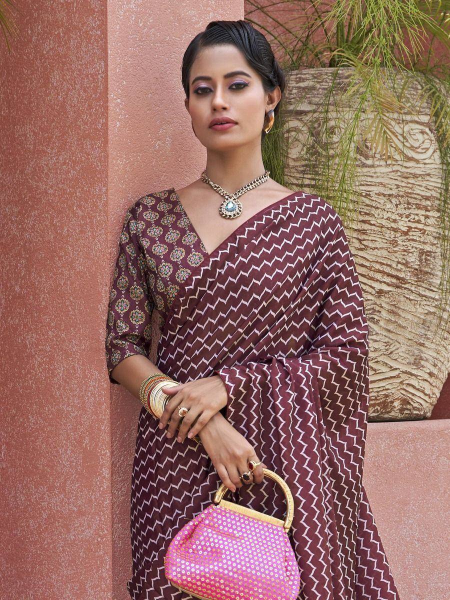 Woman in maroon printed saree with gold jewelry and pink sequin handbag, ethnic Indian wear