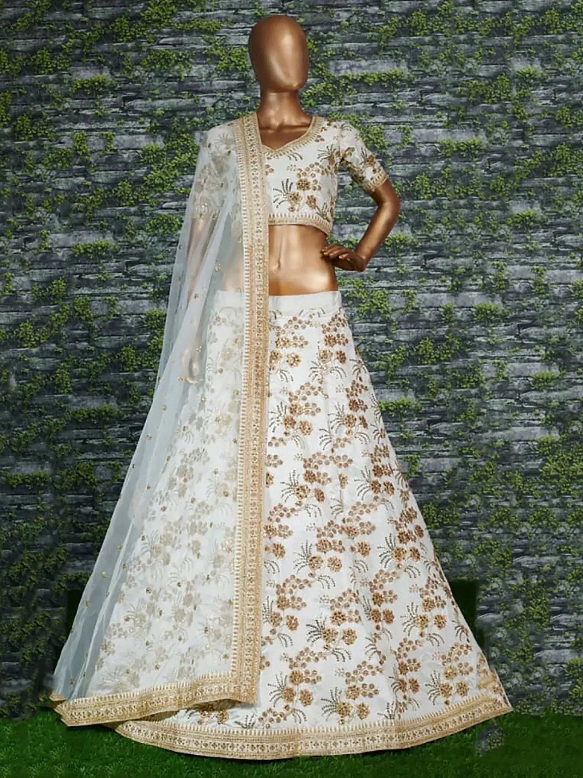 White and gold embroidered lehenga choli with sheer dupatta, displayed on mannequin against stone wall