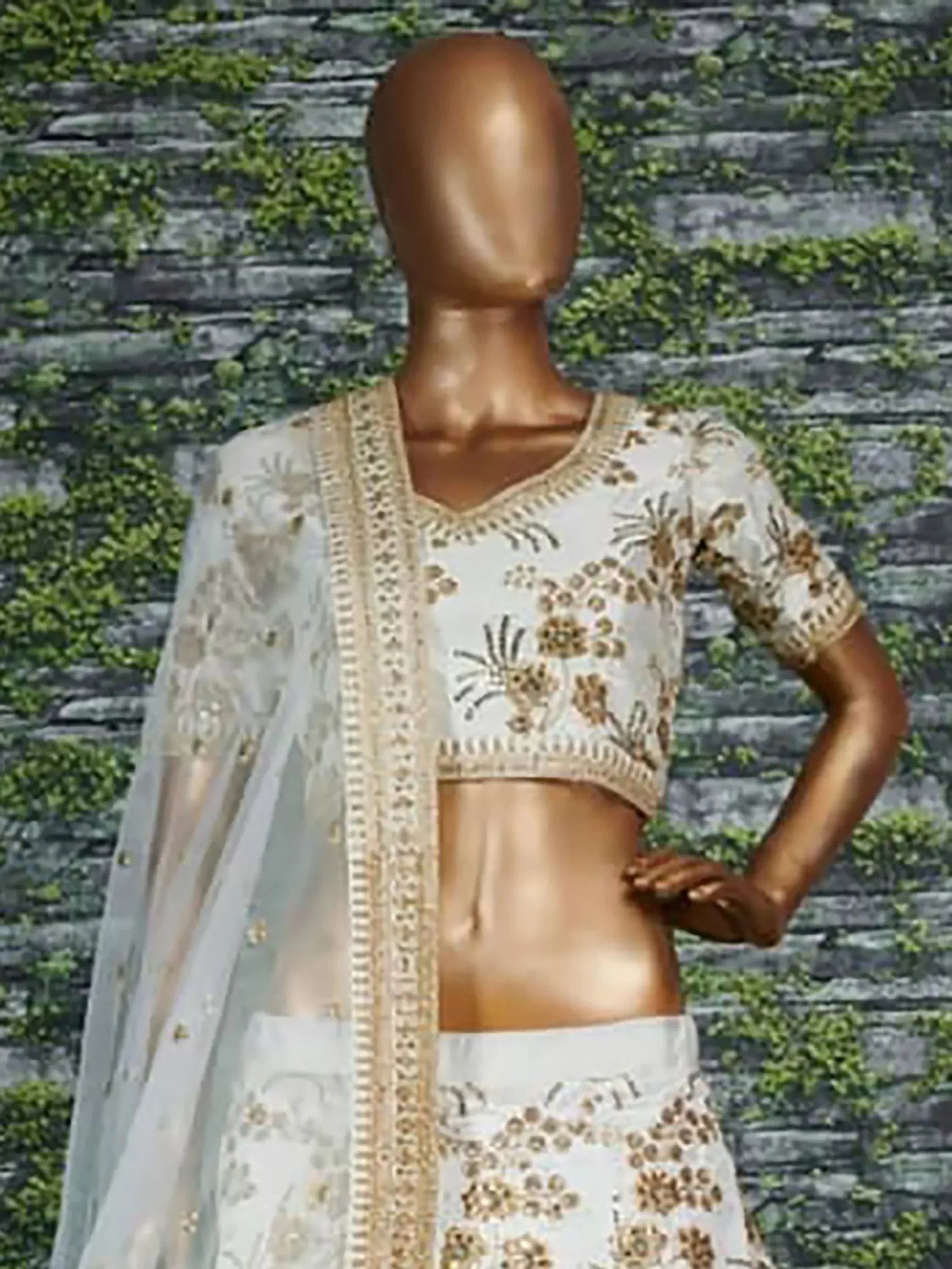 White and gold embroidered lehenga choli with dupatta, displayed on mannequin against stone wall