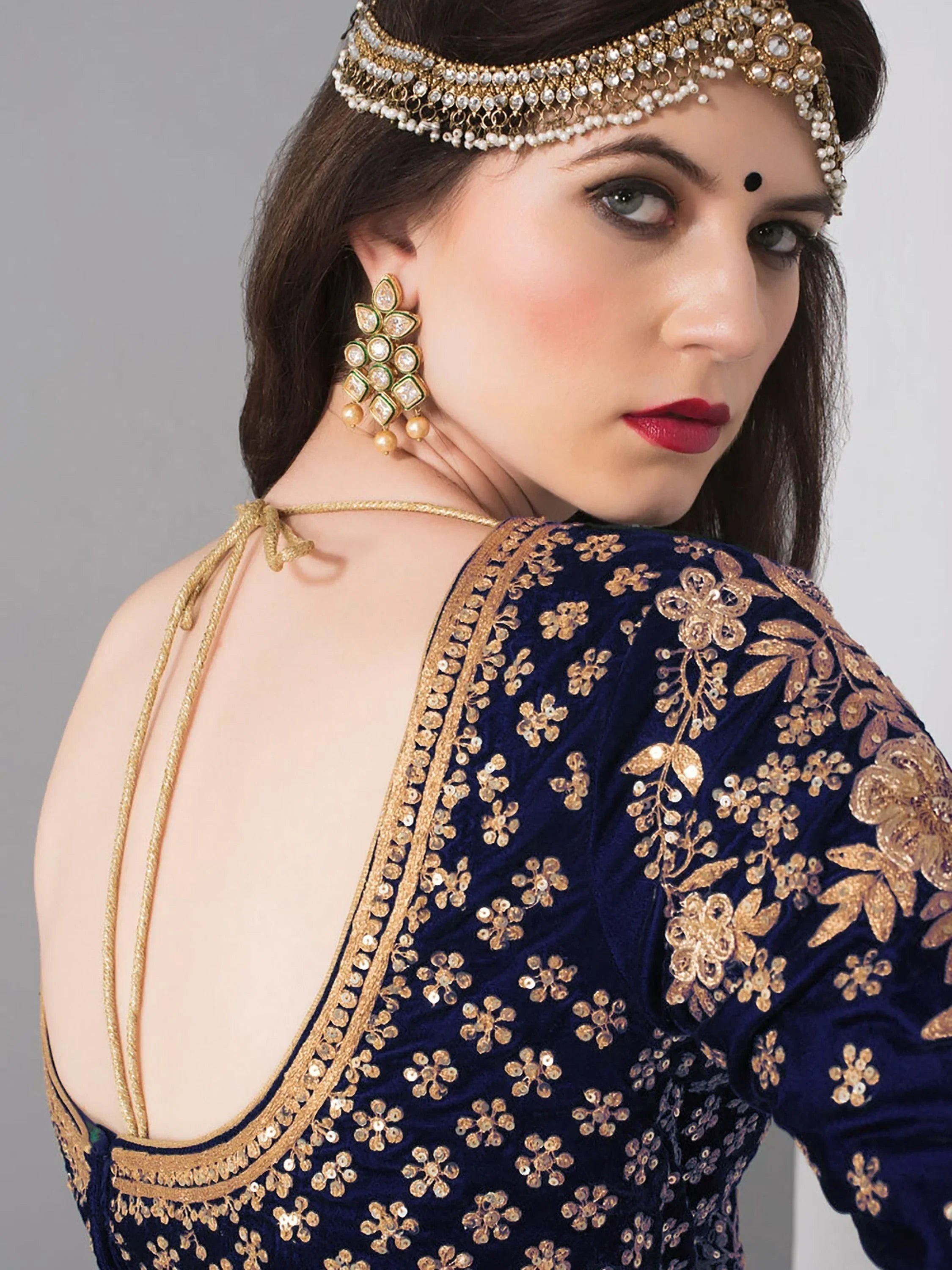 Blue velvet ethnic gown with gold floral embroidery, backless design, and traditional Indian jewelry
