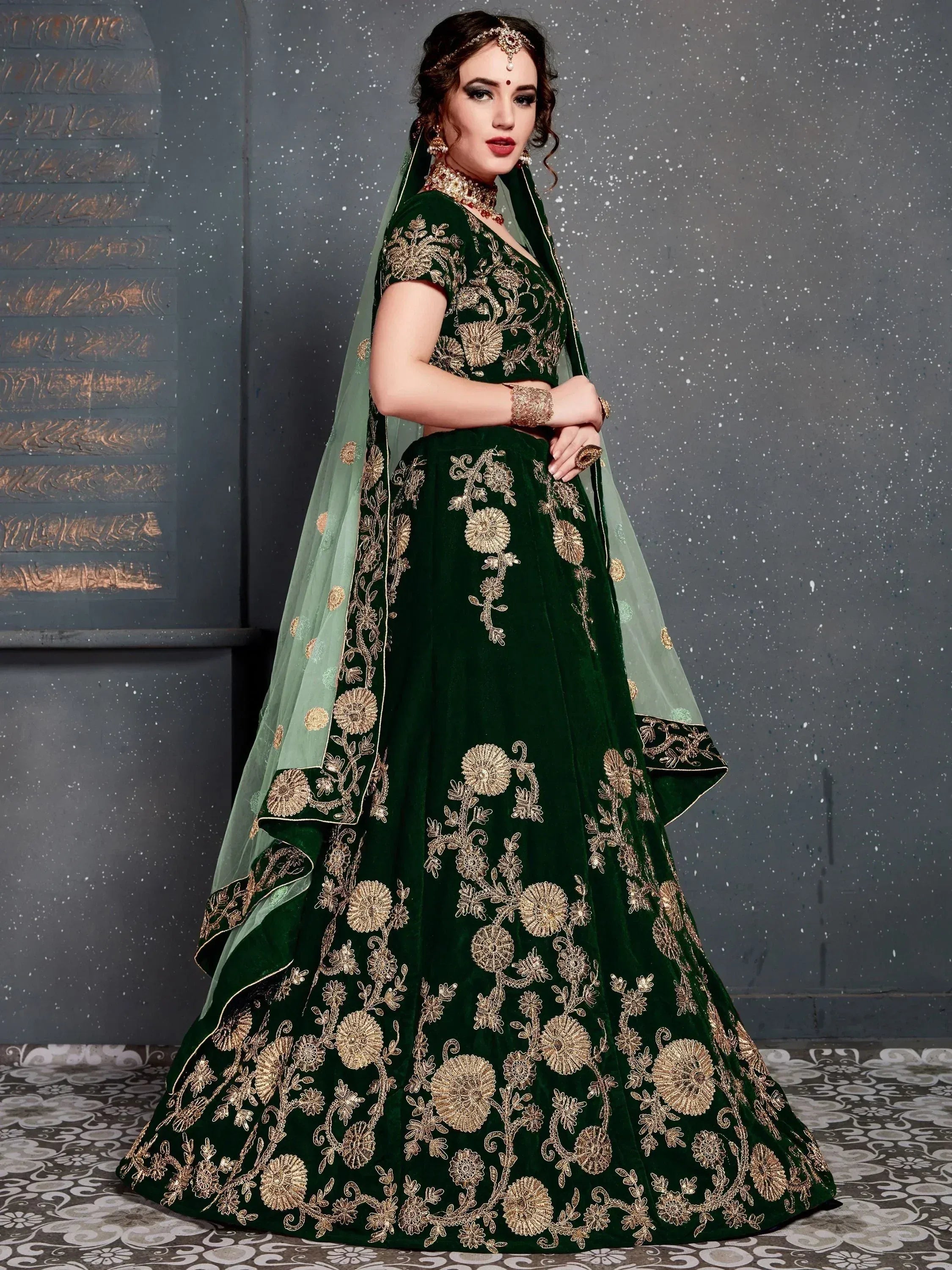 Emerald green velvet lehenga choli with gold floral embroidery and sheer dupatta, perfect for Indian weddings and festive occasions.
