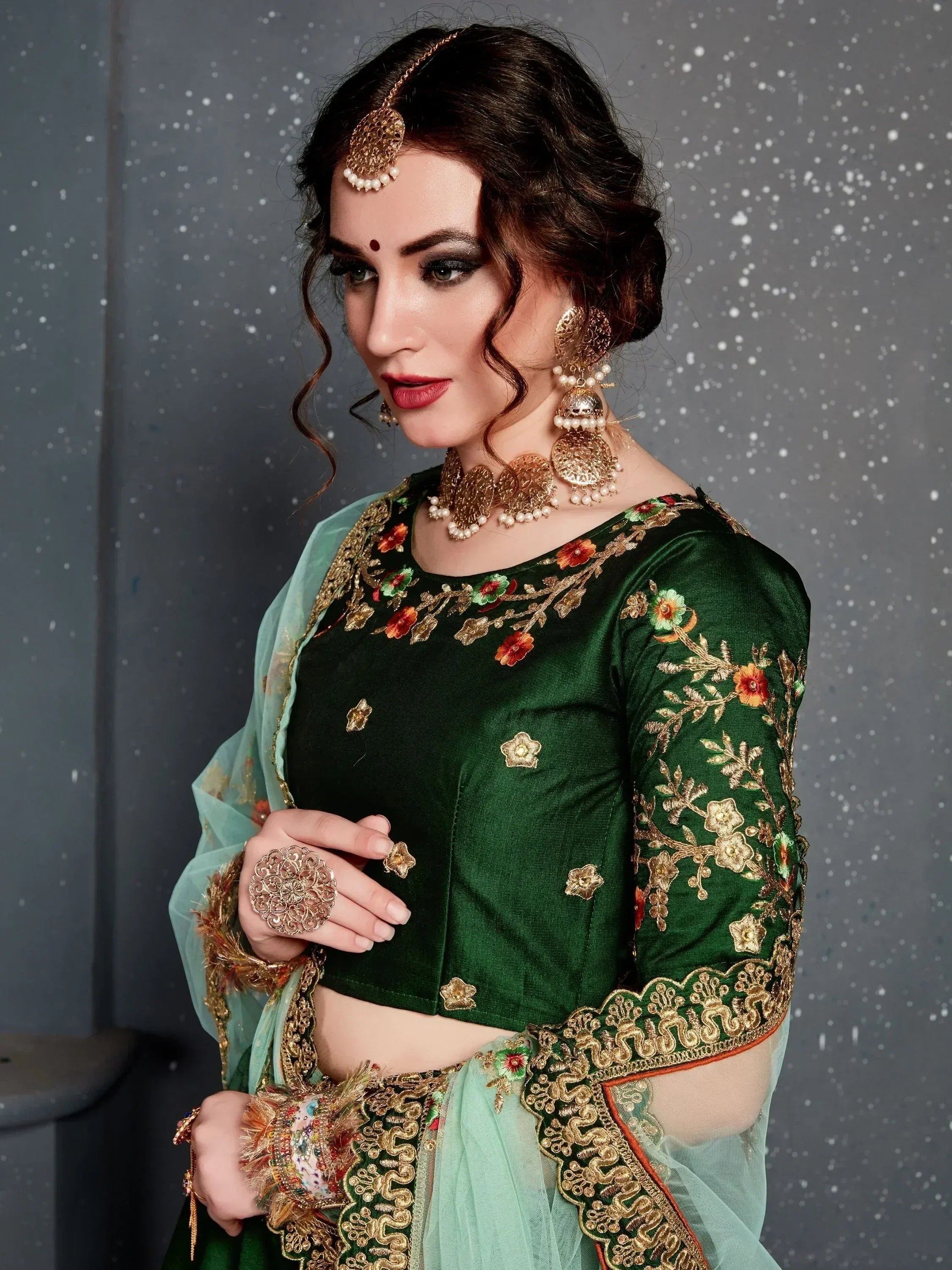 Emerald green embroidered lehenga choli with gold floral work, paired with statement jewelry for Indian ethnic wear.