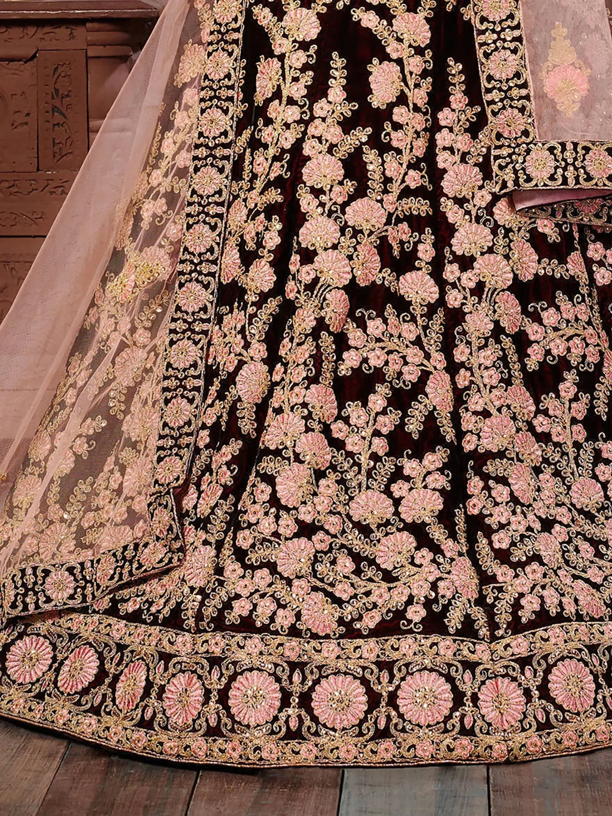 Luxury maroon velvet lehenga with pink and gold floral embroidery, perfect for Indian weddings and festive occasions.