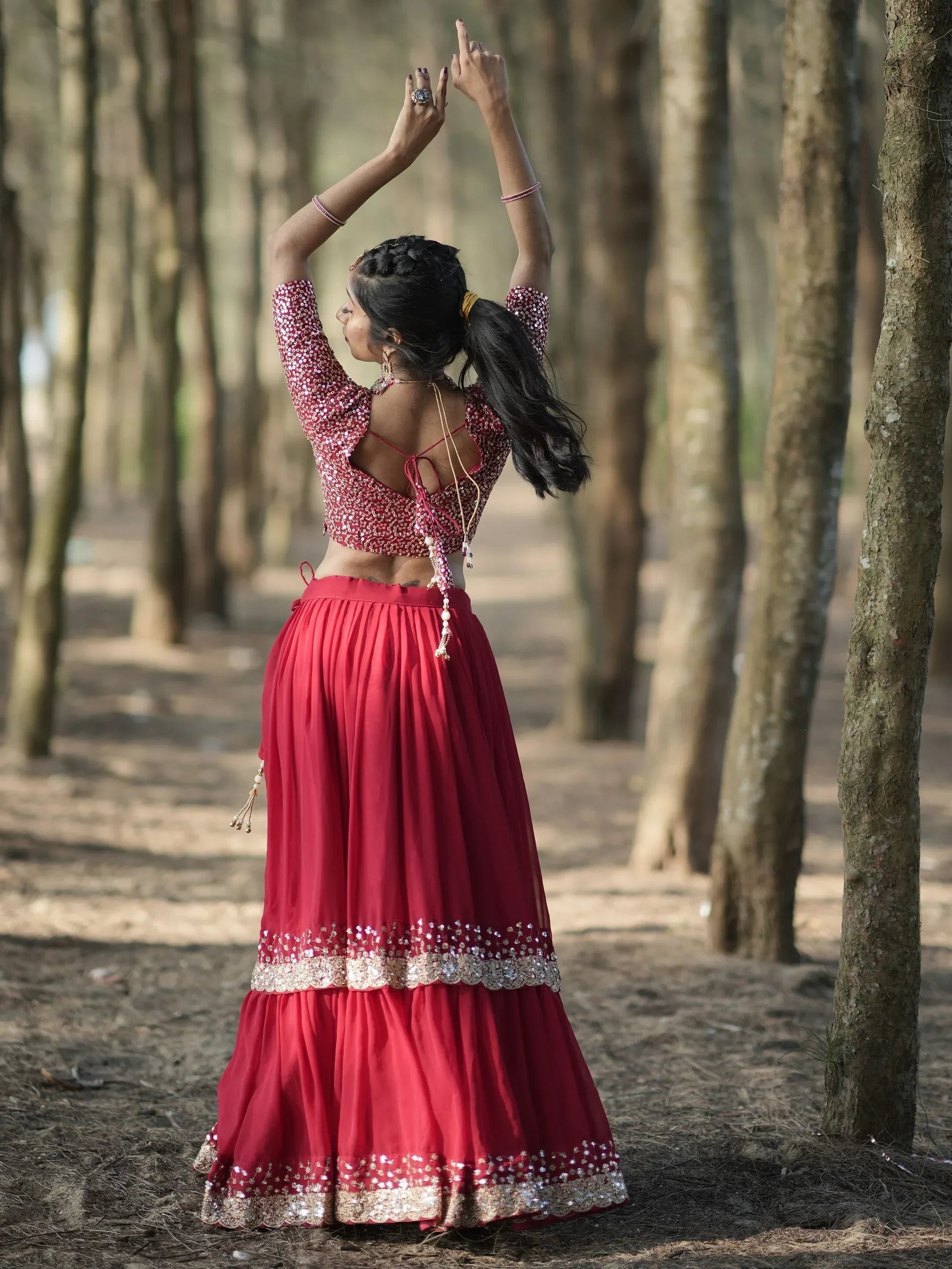 Woman in red sequin lehenga choli dancing in forest, back view with open back blouse and pleated skirt
