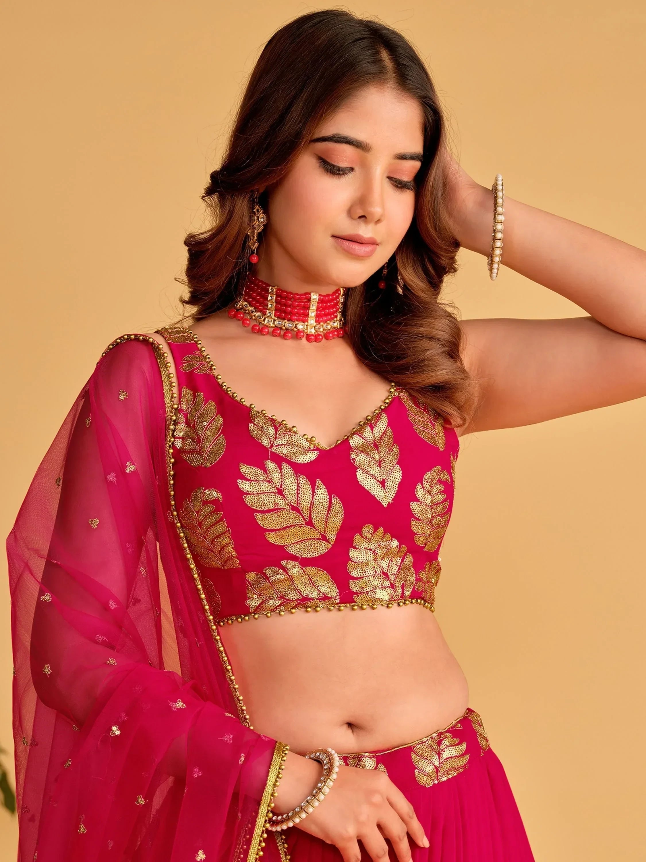 Pink lehenga choli with gold leaf embroidery, sheer dupatta, and red jewelry for Indian ethnic wear