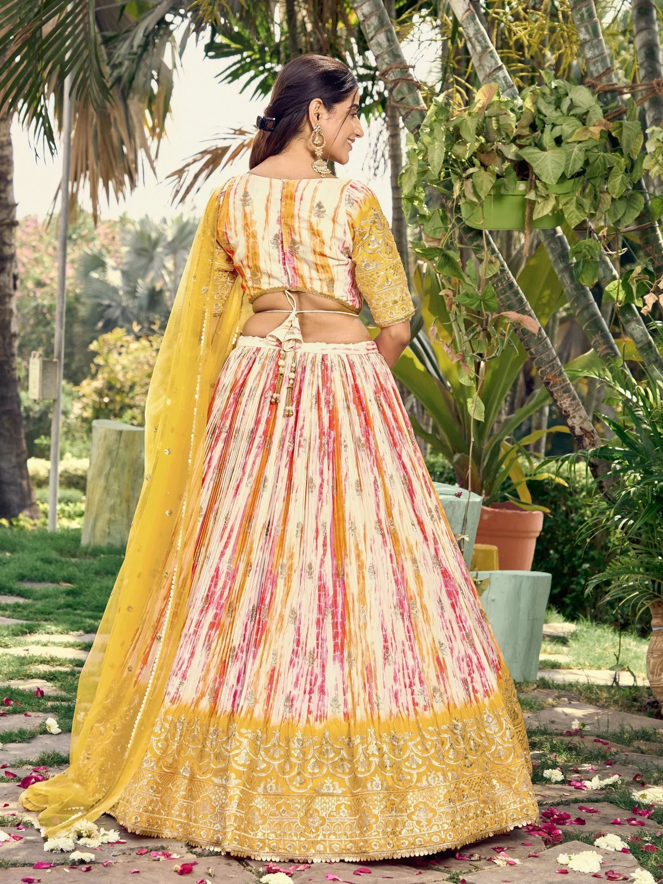 Woman in vibrant yellow and pink tie-dye lehenga choli with gold embroidery, perfect for Indian ethnic occasions